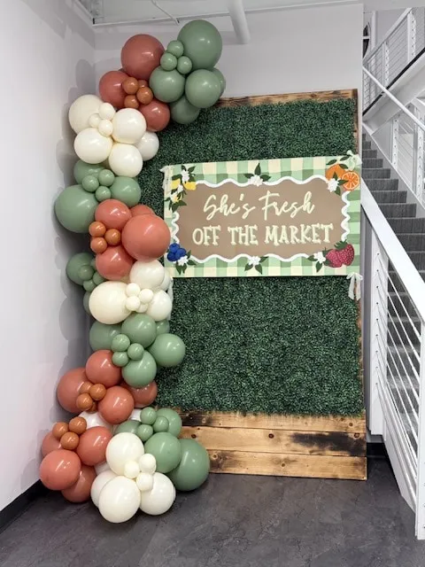 Sage, terracotta and cream garland beside a greenery wall for a market-themed shower